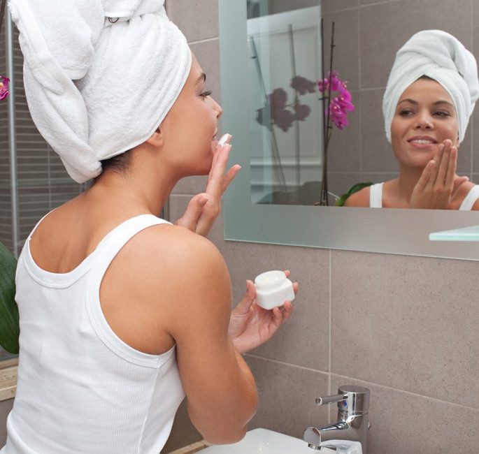 Mulher fazendo rotina de skin care em frente ao espelho